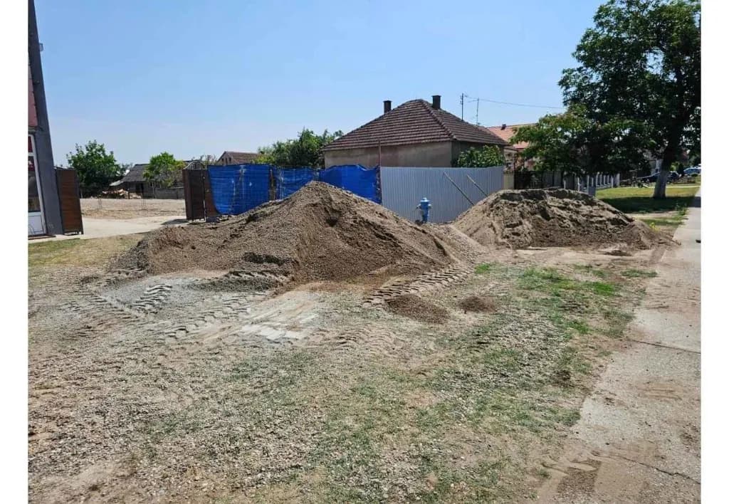 Gradilište firme SB GRADNJA u Sremskoj Mitrovici — nasipi šljunka i peska, tragovi radne mašine i priprema terena za izvođenje građevinskih radova